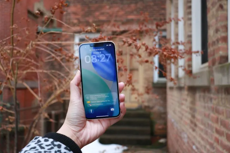 The iPhone 17e held up in mid-air in front of some red foliage.