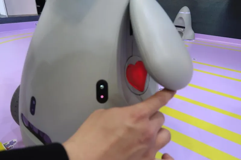 A hand is seen lifting OlloBot's arm to reveal a red heart underneath, which serves as a removable module that contains its data