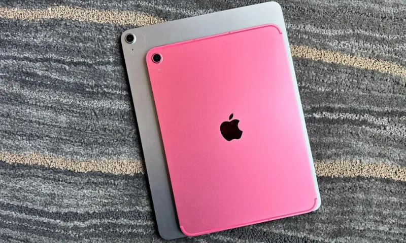 Розовый Apple iPad (A16) на подлокотнике светло-коричневого кожаного кресла, нижним краем к камере, демонстрируя тонкий профиль устройства с решётками динамиков и портом USB-C.
