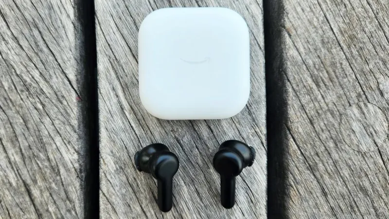 Черные беспроводные наушники-вкладыши лежат на столешнице темно-серого цвета под их трубчатым зарядным кейсом. На кейсе и наушниках отображается логотип Skullcandy, а на кейсе есть встроенный серебряный зажим.